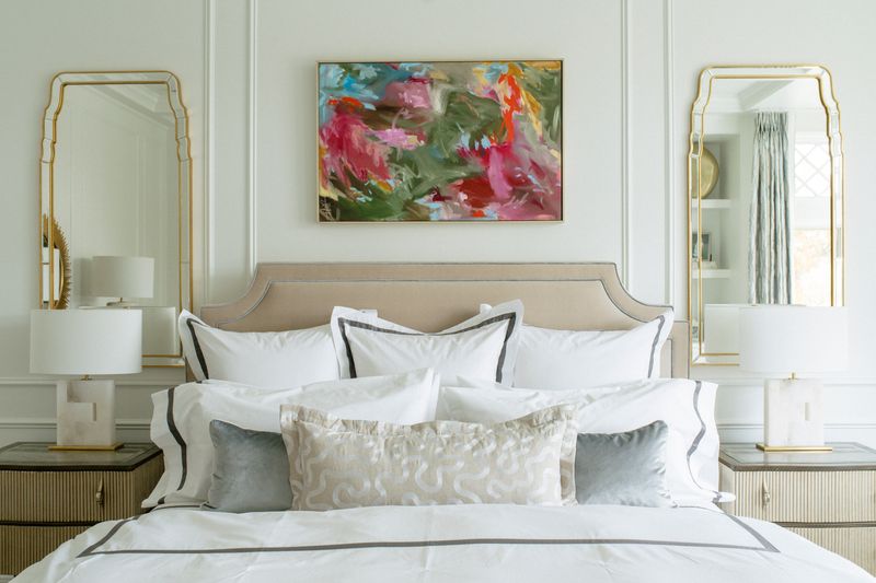 A primary bedroom in Des Moines with a linen upholstered headboard under a bright abstract painting.