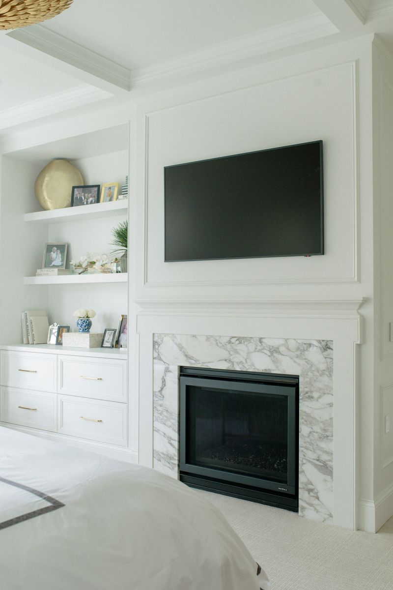A primary bedroom in Des Moines with a marble fireplace surround set into a white paneled wall.