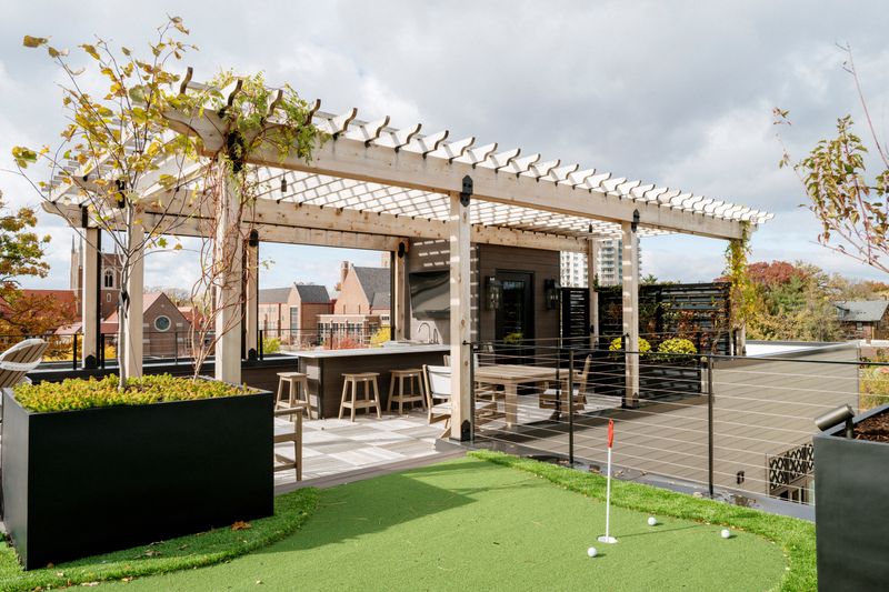 A roof terrace in Des Moines with a cedar pergola over a dark outdoor bar, set on artificial turf.