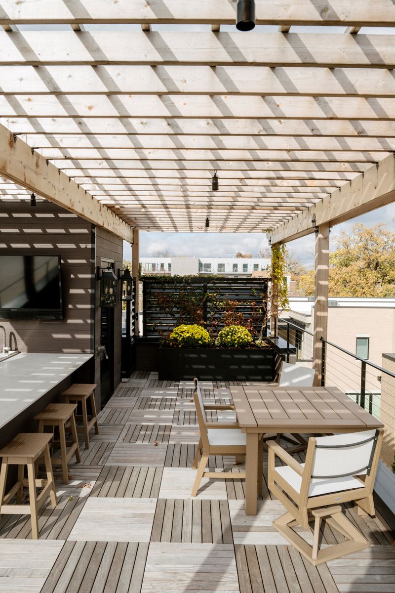 A rooftop deck in Des Moines with a cedar pergola over a white counter bar and teak stools.