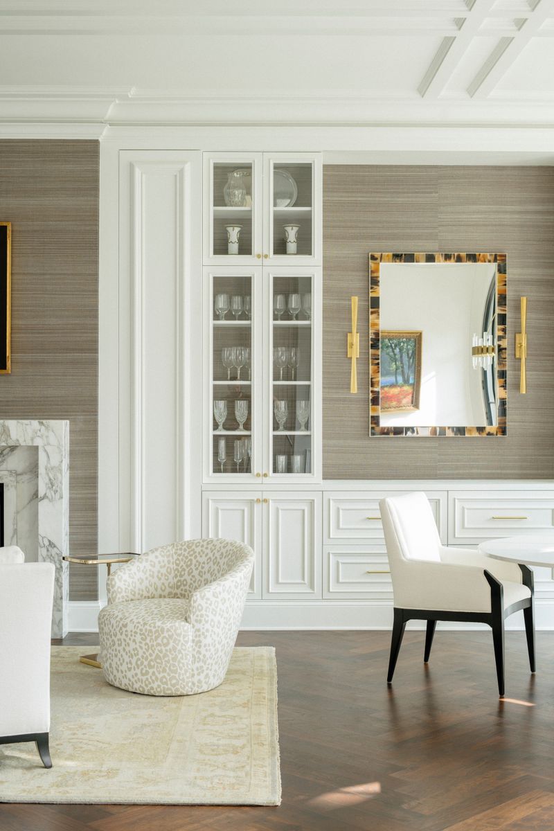 A sitting room in Des Moines with a leopard print swivel chair on herringbone wood floors by a white built in cabinet.