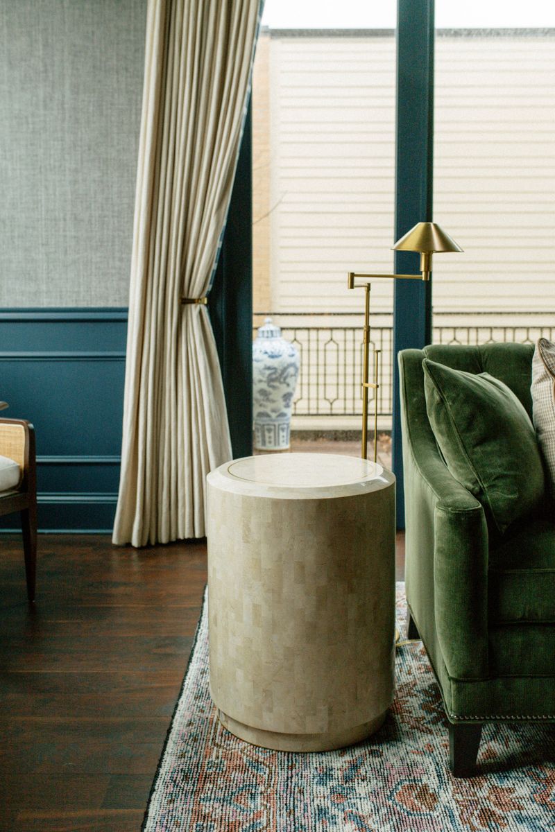 A sitting room in Des Moines with a green velvet sofa beside a stone drum table and a brass floor lamp.