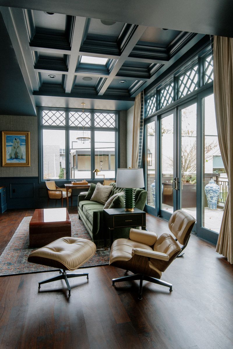 A study in Des Moines with a dark teal coffered ceiling above a green velvet sofa and leather lounge chair.