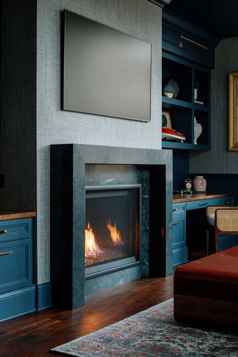 A navy blue study in Des Moines with a dark soapstone fireplace surround set into a grasscloth wall.