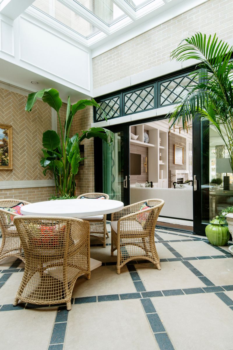 A brick sunroom in Des Moines with woven wicker chairs around a white oval table on inset tile floors.