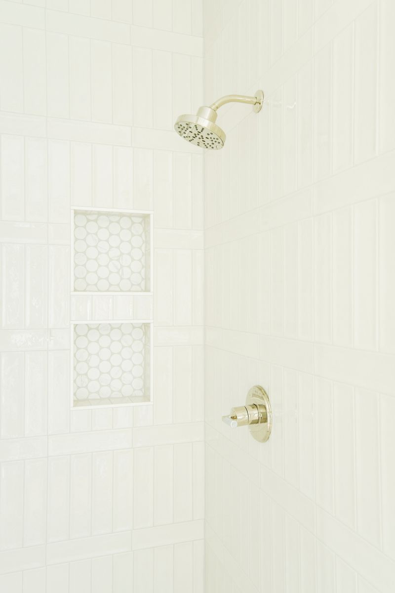A white tile shower in Clive with penny round niches and a polished nickel shower head.