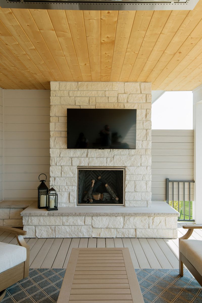 A covered porch in Clive with a cream limestone fireplace under a knotty pine plank ceiling.