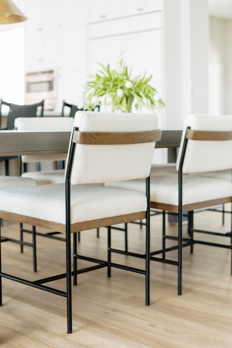 A dining room in Clive with cream boucle chairs on black metal frames beside a dark wood table.