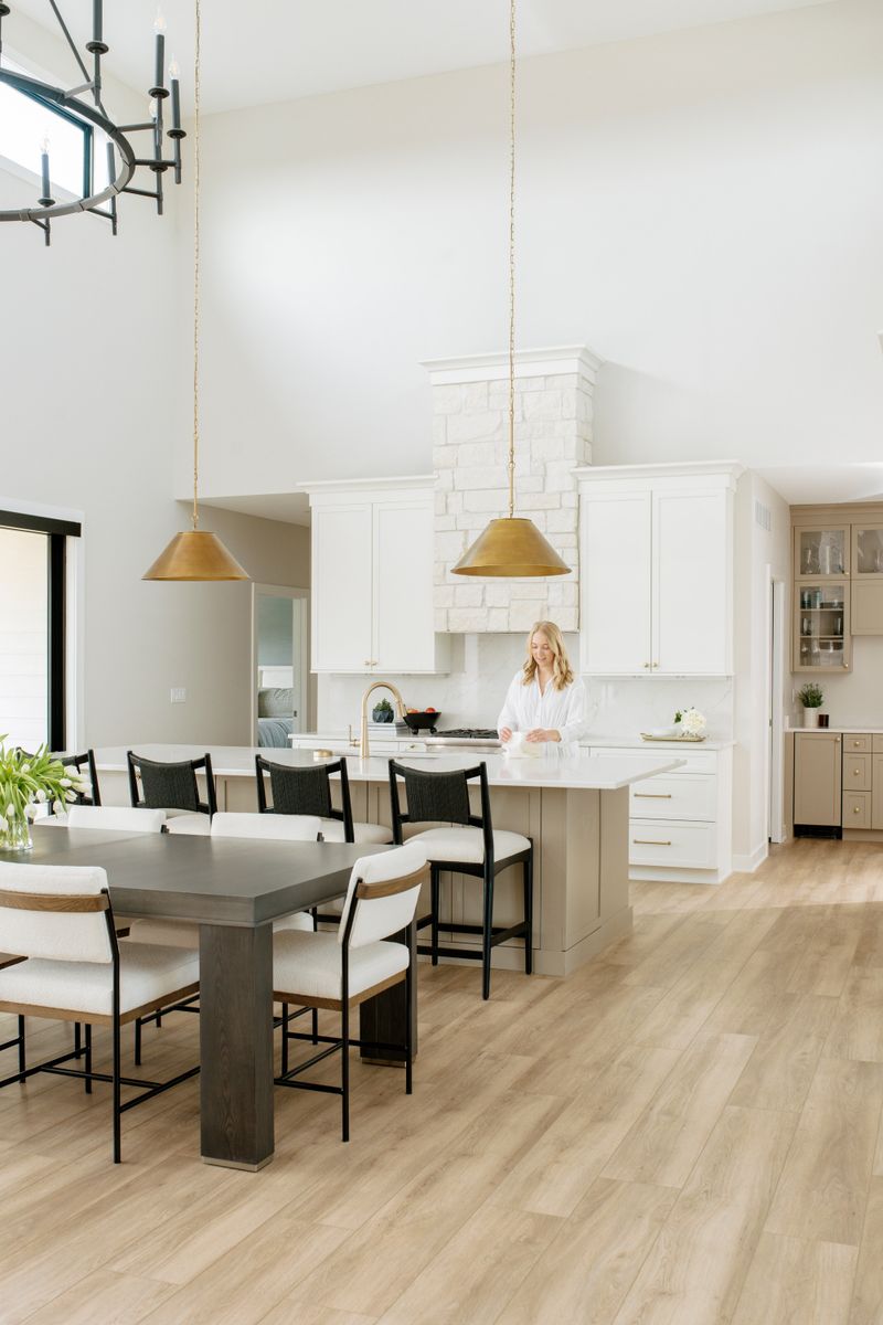 A white kitchen in Clive with a limestone hood over the range and brass pendants above the island.