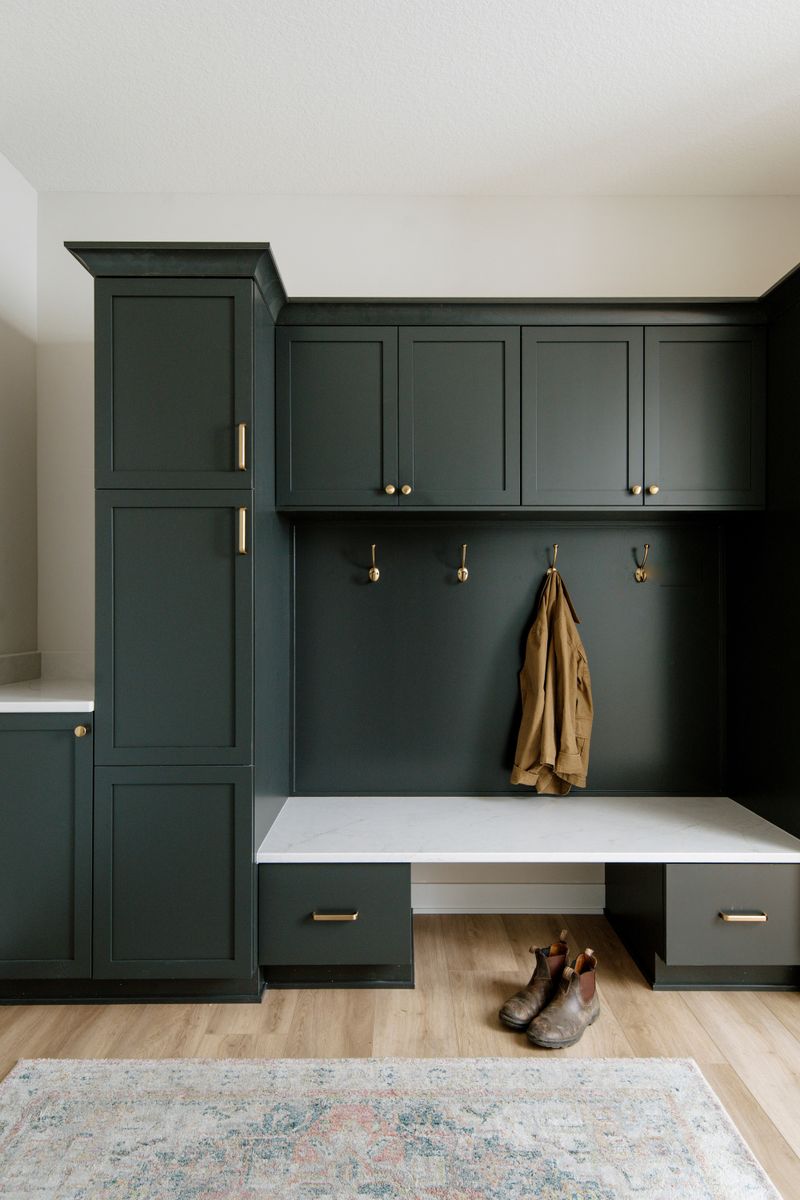 A dark green mudroom in Clive with a white marble bench seat and brass coat hooks.