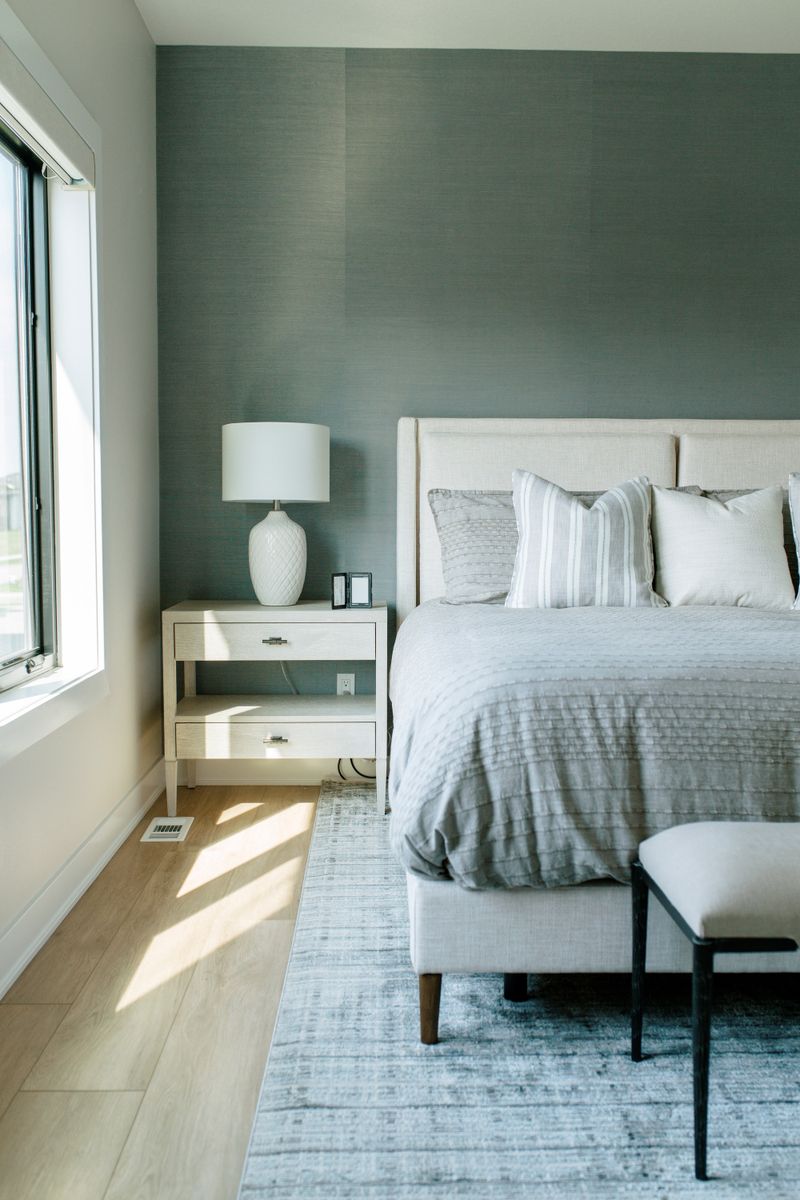 A primary bedroom in Clive with a green grasscloth accent wall behind a cream upholstered bed and pale oak floors.