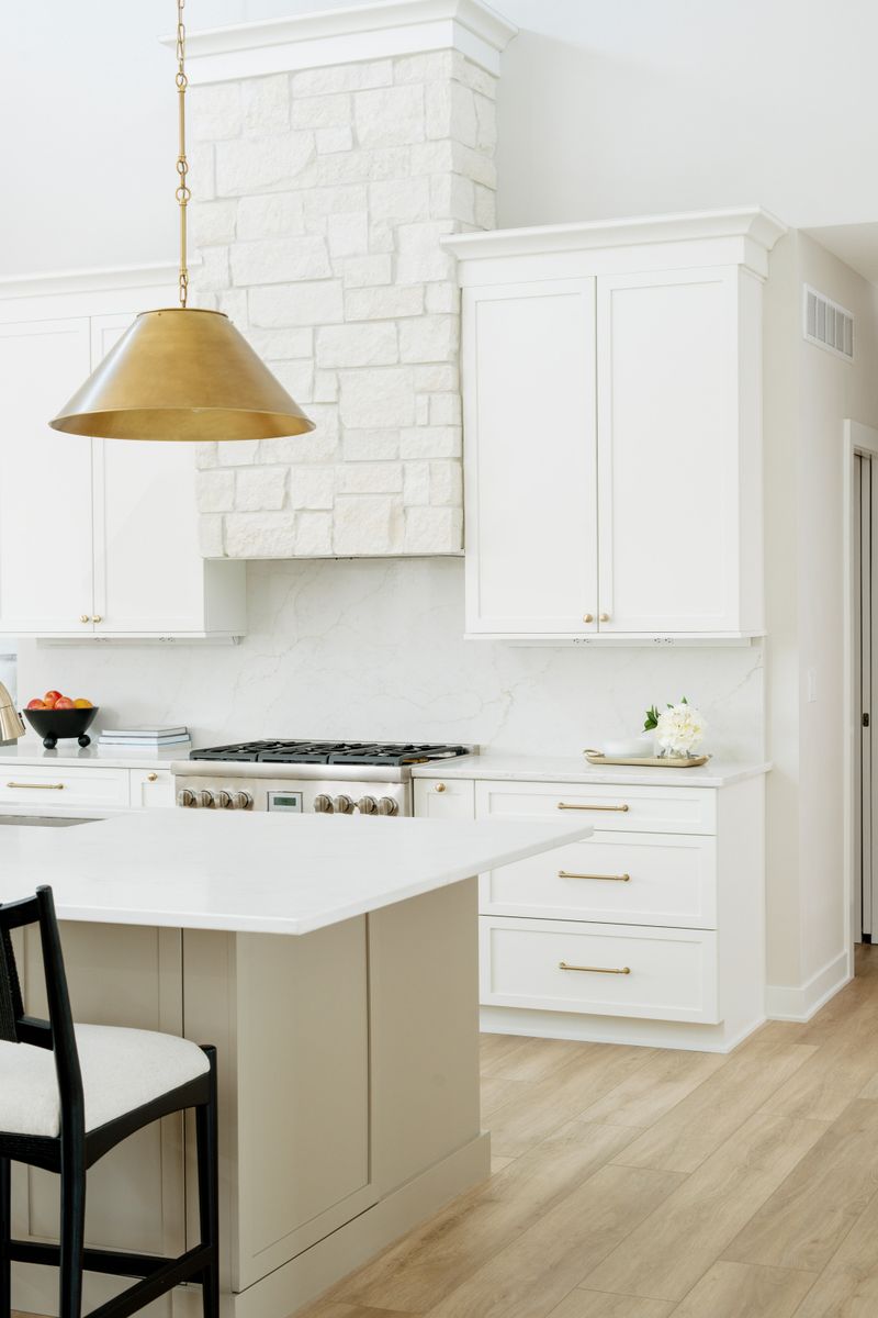 A white kitchen in Clive with a white stone hood over the range and a marbled quartz backsplash.