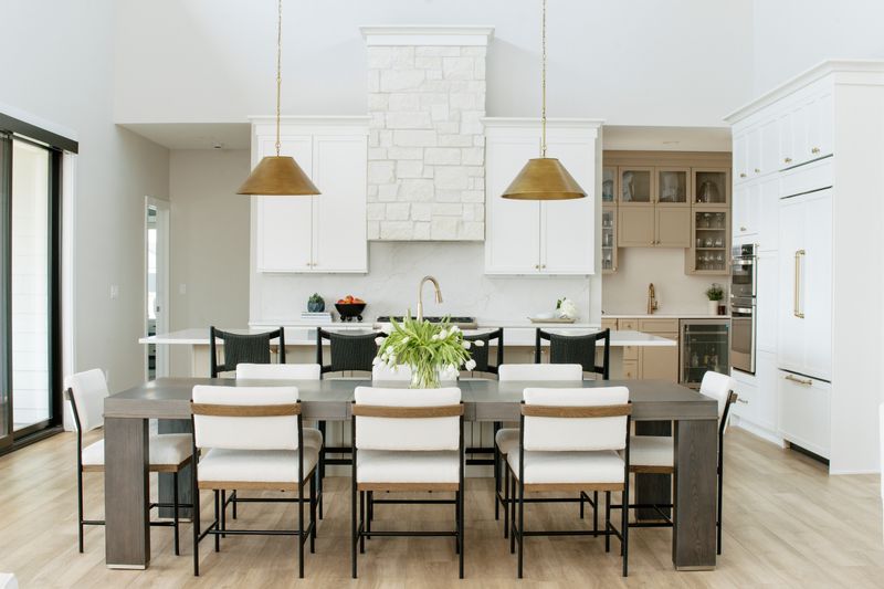 A white kitchen in Clive with a white stone range hood set between a pair of aged brass dome pendants.