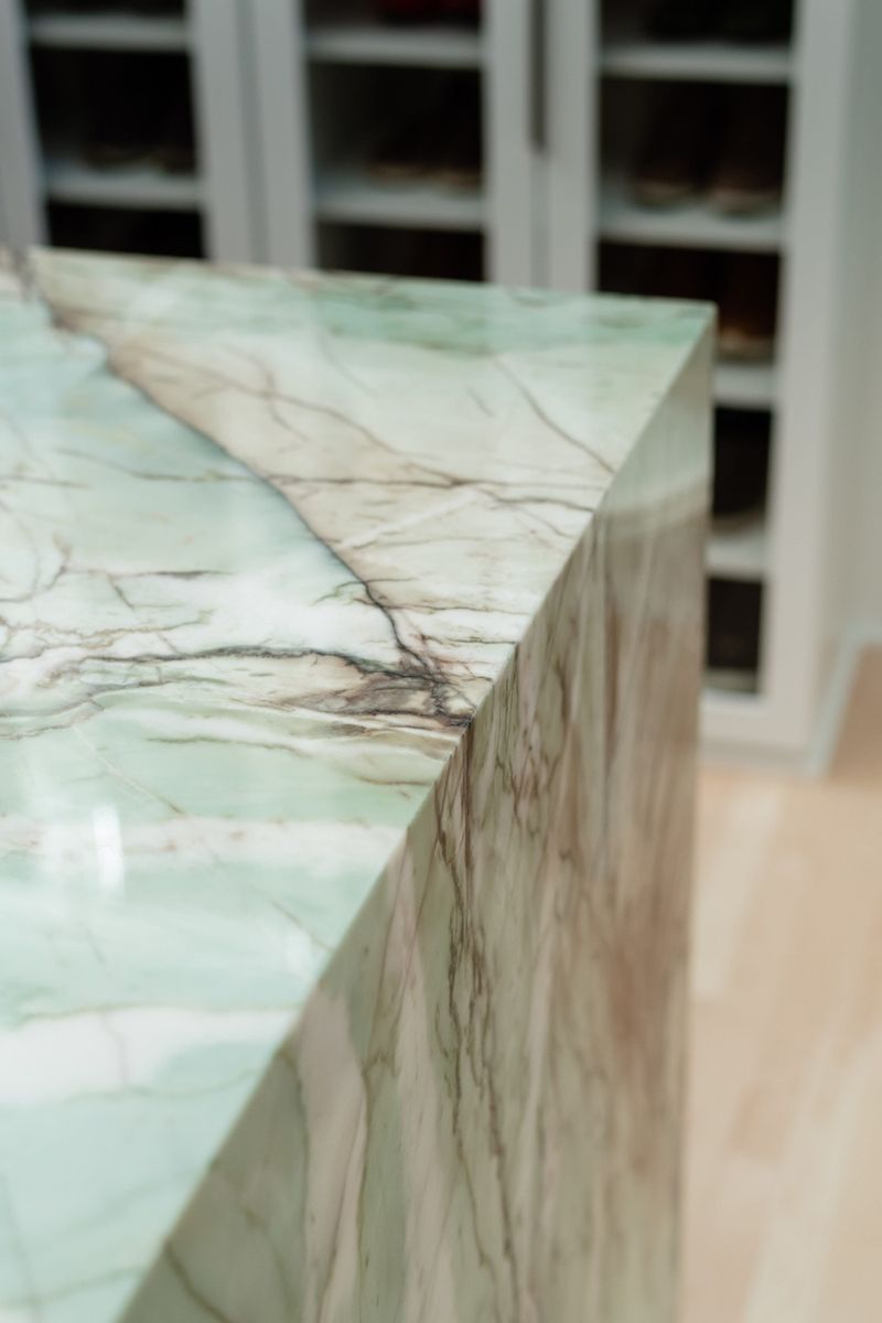 A Des Moines kitchen island with a green veined marble waterfall edge, set against white glass cabinets.