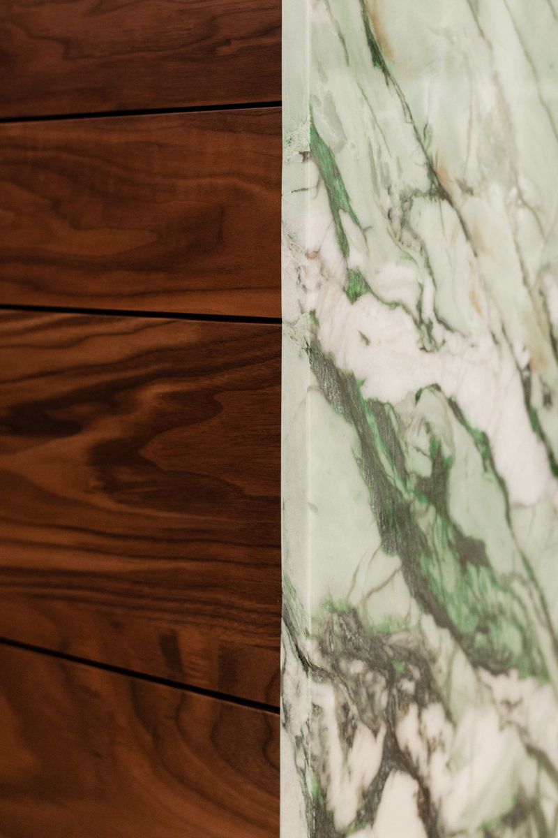 Green veined marble meeting flat walnut drawer fronts in a Des Moines kitchen, with a mitered stone edge.