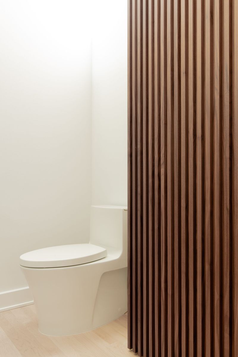 A powder room in Des Moines with a walnut slat wall screening the toilet from the white plaster walls.
