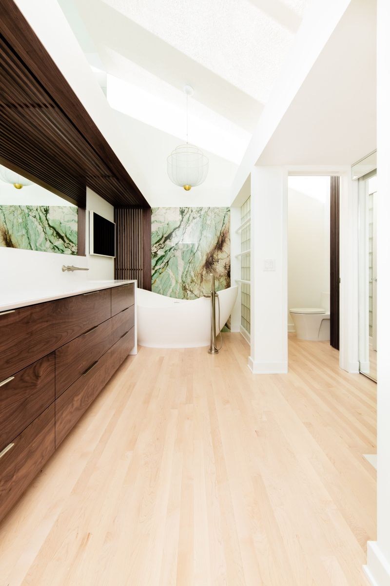 A primary bath in Des Moines with a green marble wall behind the freestanding tub and walnut vanity cabinets.