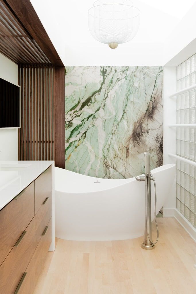 A primary bath in Des Moines with a freestanding tub against a green veined stone slab wall.