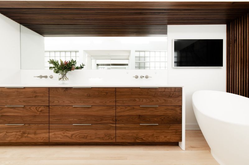 A primary bath in Des Moines with a walnut double vanity under a slatted wood ceiling and white quartz counter.