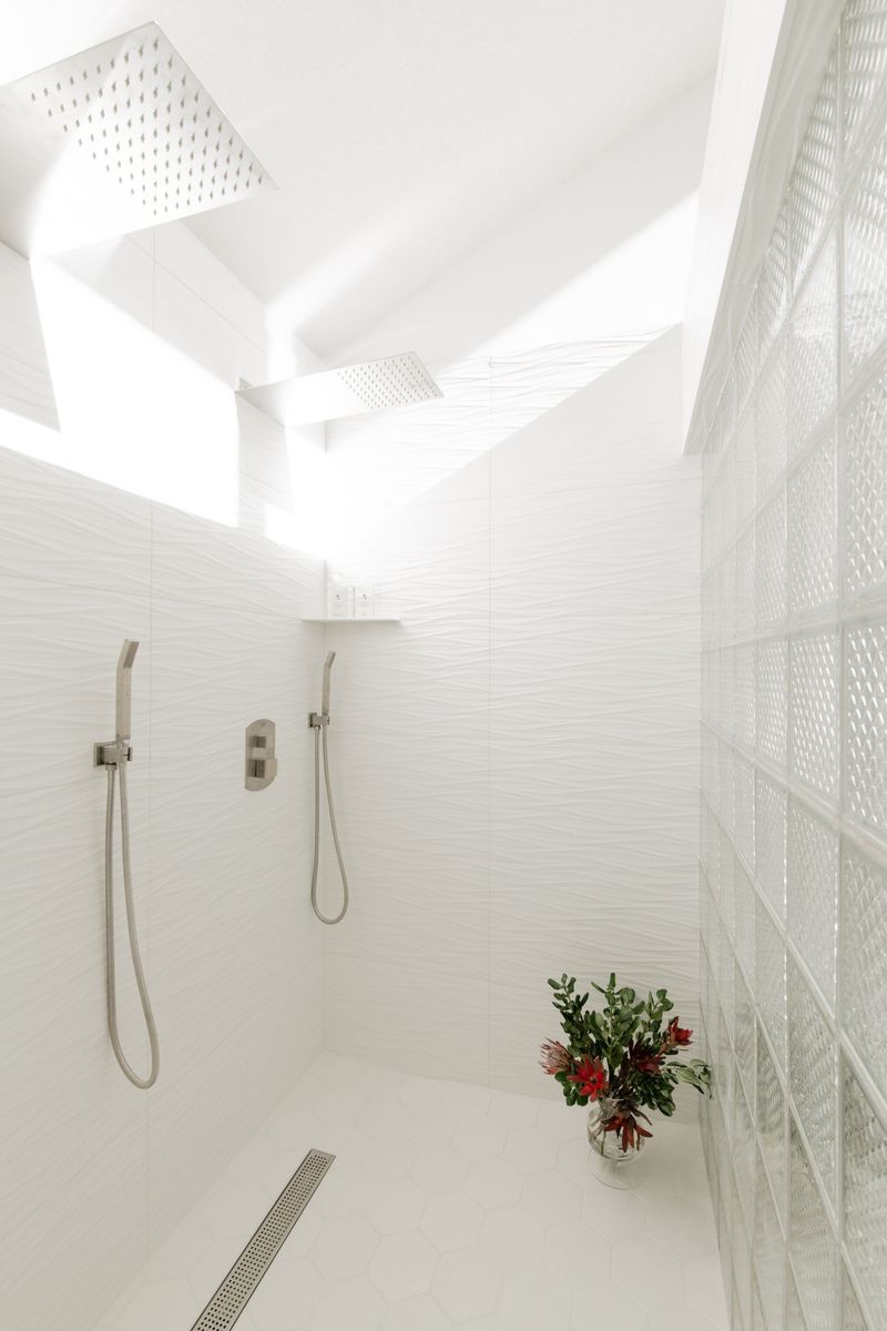 A primary bath shower in Des Moines with wavy white tile and two square rain heads set into the ceiling.