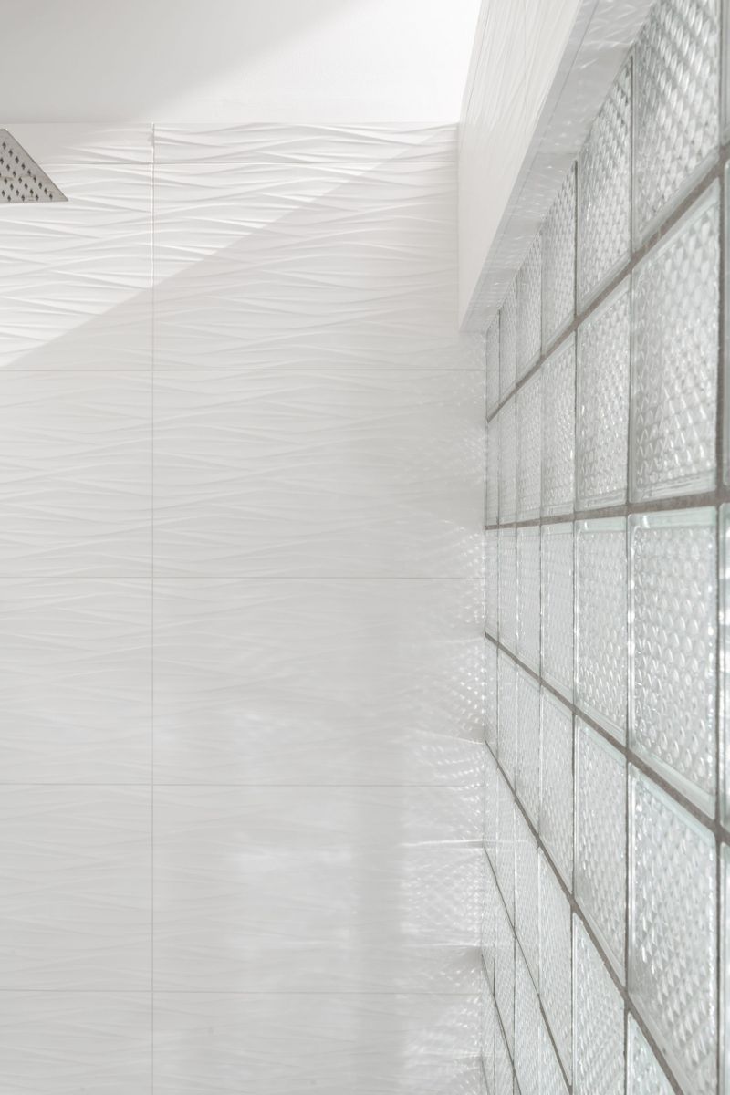 A Des Moines shower with a glass block wall beside white wavy tile and a square rain shower head.