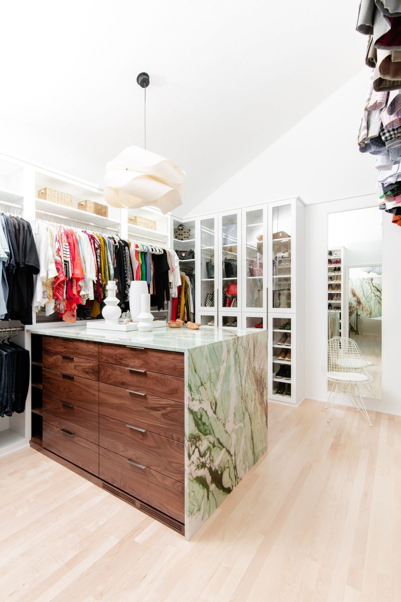 A walk in closet in Des Moines with a green marble waterfall island over walnut drawers.