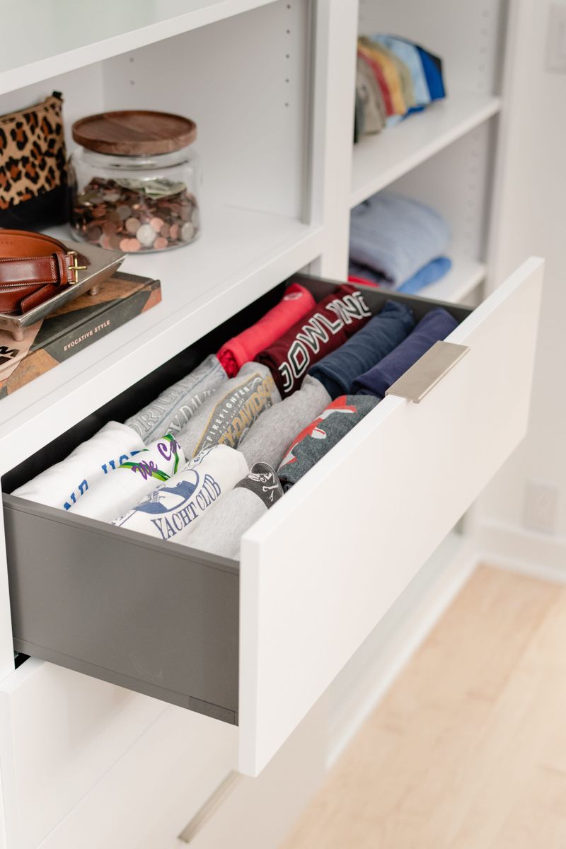 A white walk in closet in Des Moines with a brushed nickel pull on a gray lined drawer for folded shirts.