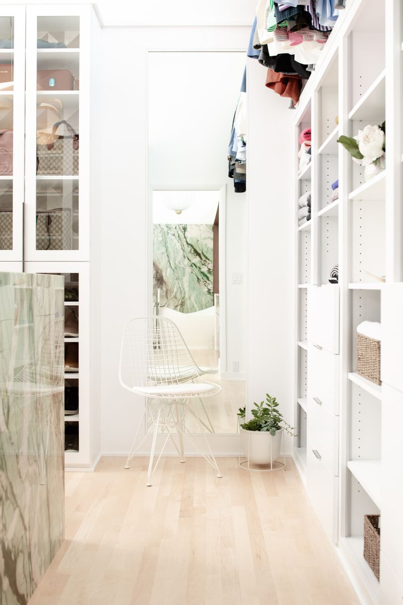 A white walk in closet in Des Moines with a full length mirror and a green marble island under glass front cabinets.