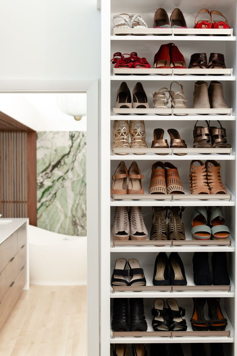 A walk in closet in Des Moines with white built in shoe shelving looking through to a green marble bath wall.