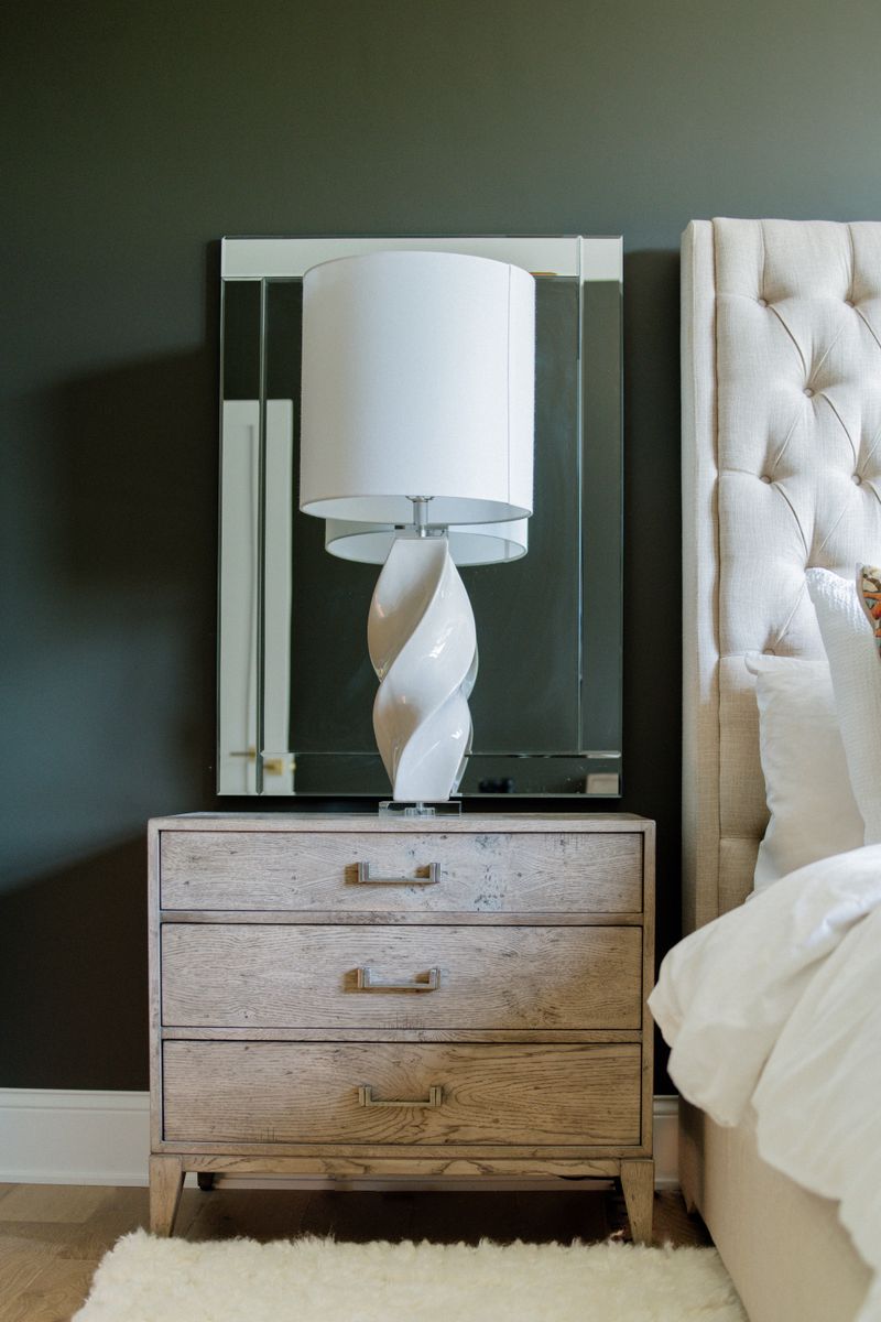A dark green bedroom in West Des Moines with a white twisted ceramic lamp on a light oak nightstand.