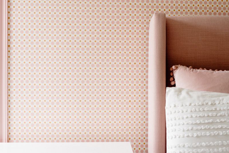 A bedroom in West Des Moines with a pink linen wingback headboard against pink and gold star wallpaper.