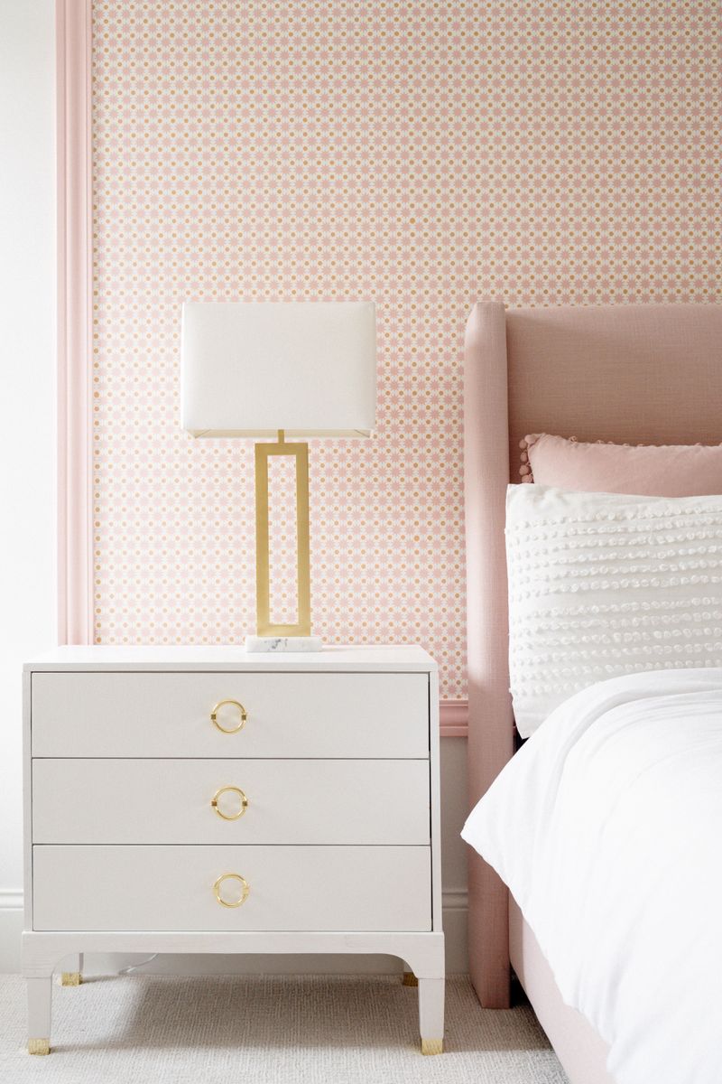 A bedroom in West Des Moines with pink patterned wallpaper behind a blush upholstered headboard.
