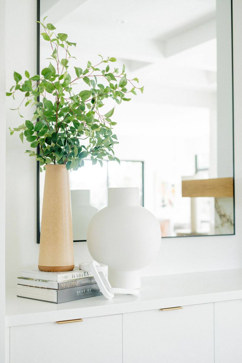 An entry in West Des Moines with a black framed mirror above a white console styled with ceramic vases.