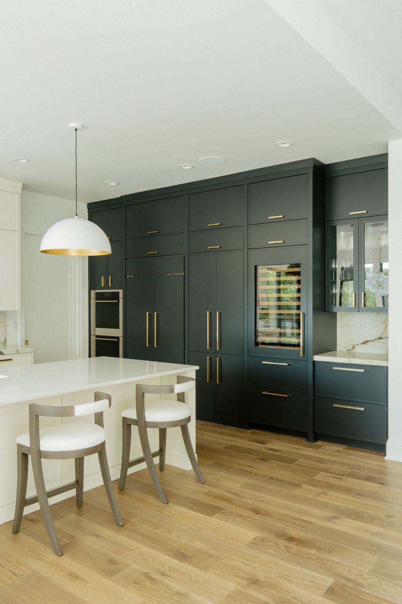 A kitchen in West Des Moines with a wall of dark green cabinets and long brass pulls, over white oak floors.
