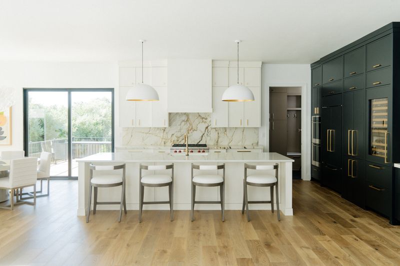 A white kitchen in West Des Moines with a gold veined marble backsplash behind the range and white oak floors.