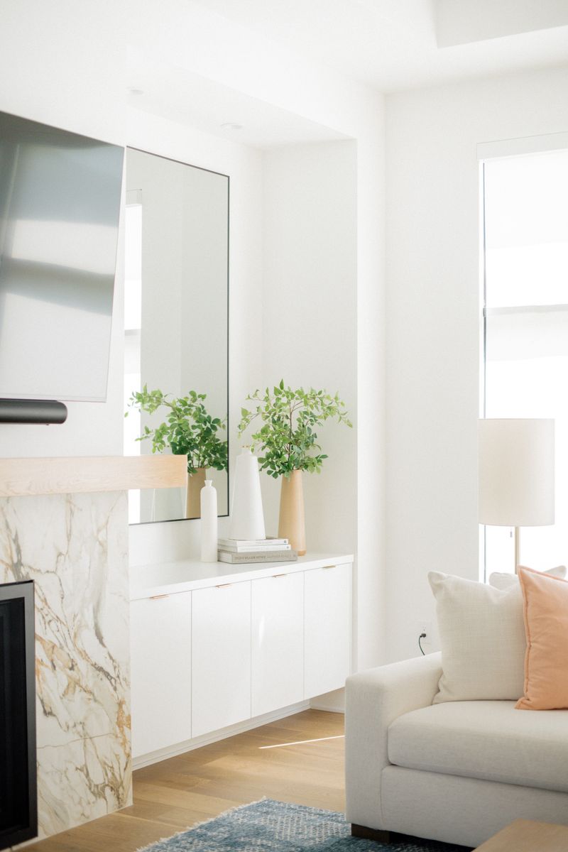 A white living room in West Des Moines with a veined marble fireplace surround under a light oak mantel.