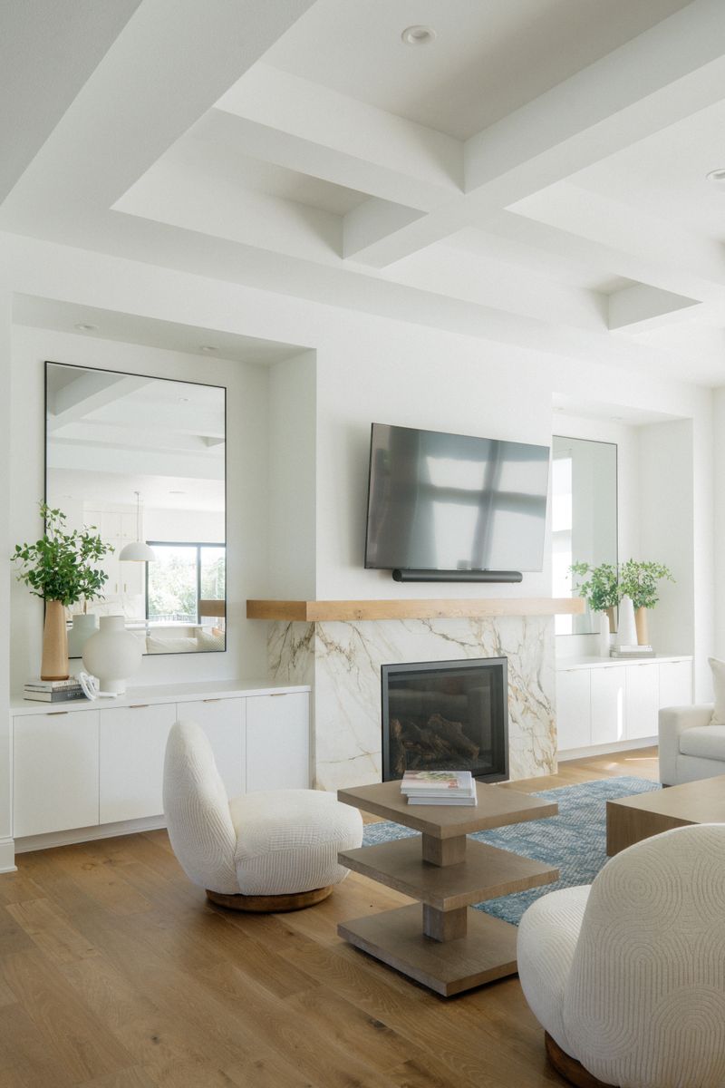 A white living room in West Des Moines with a marble fireplace under a light oak mantel and wide oak floors.