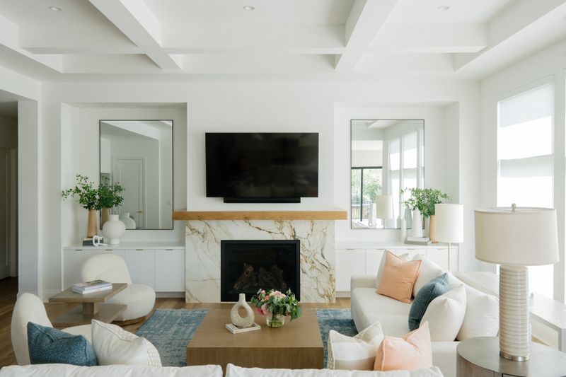 A white living room in West Des Moines with a veined marble fireplace under a light oak mantel.