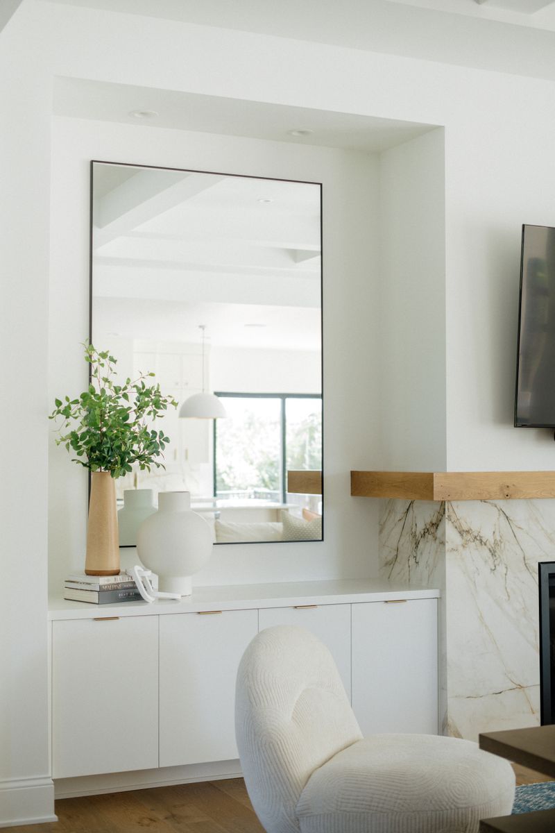 A white living room in West Des Moines with a veined marble fireplace under a chunky white oak mantel.