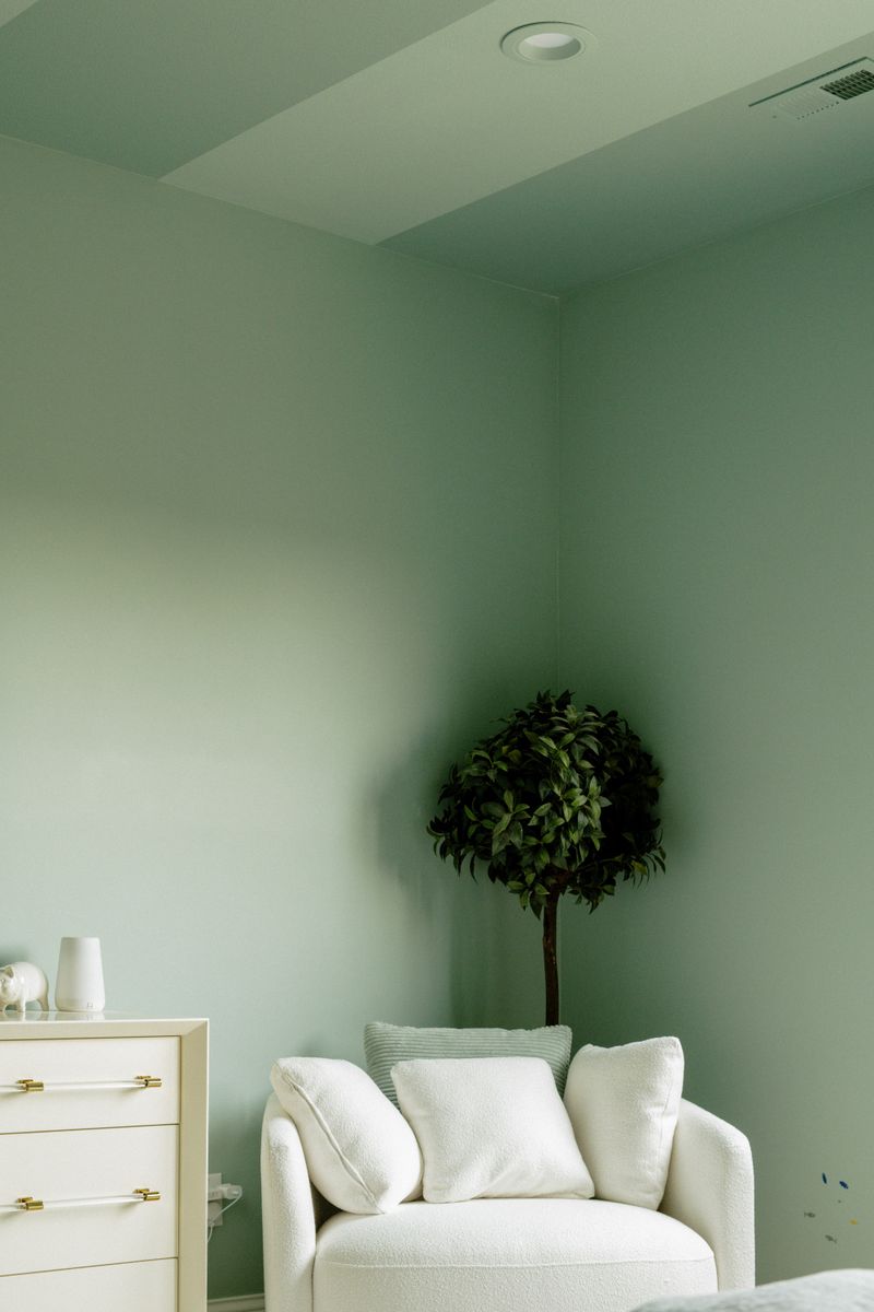A sage green nursery in West Des Moines with a white boucle glider chair in the corner.