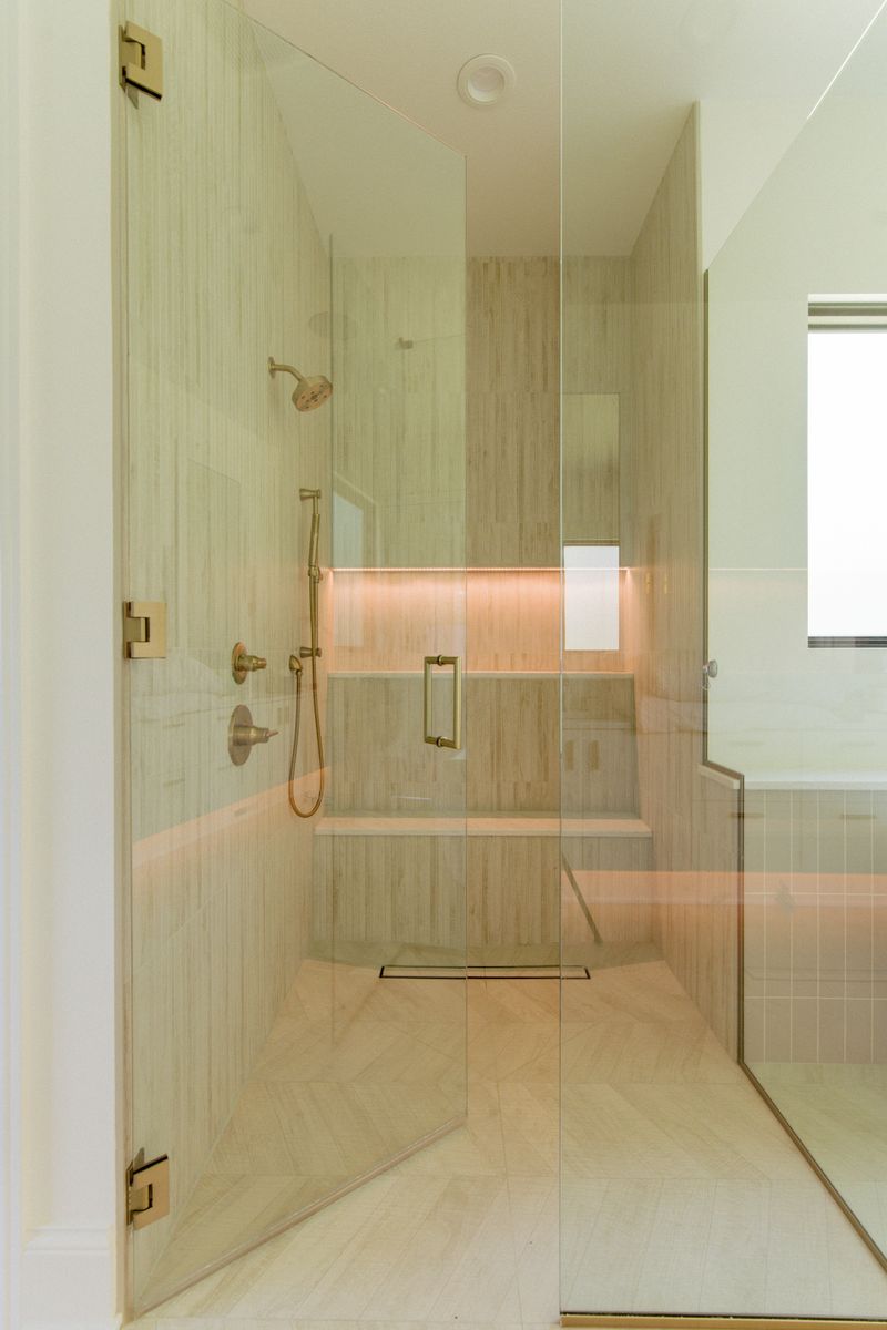 A primary bath in West Des Moines with a glass walk-in shower with LED shampoo niche and brushed brass fixtures.