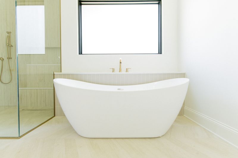 A primary bath in West Des Moines with a freestanding white soaking tub and a brass deck mounted tub filler.