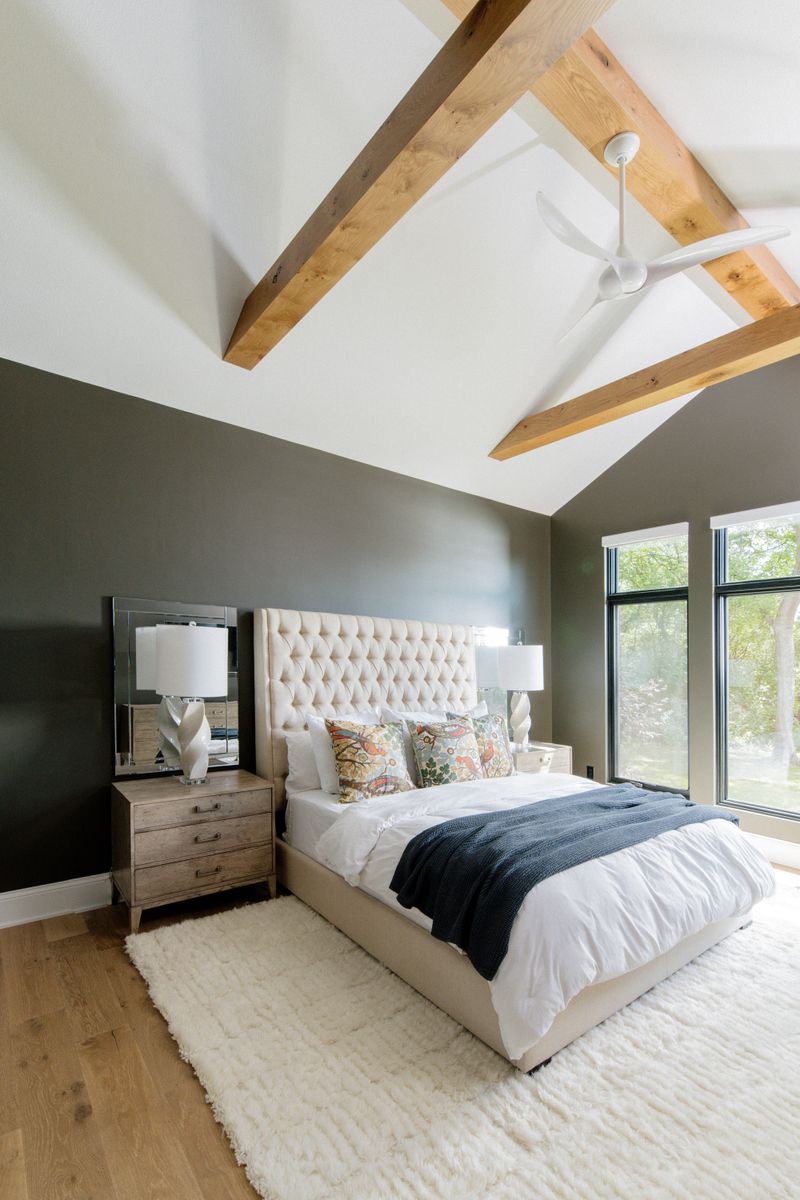 A primary bedroom in West Des Moines with oak beams on a vaulted ceiling above a deep olive accent wall.