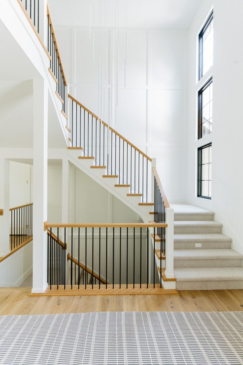 A white stairwell in West Des Moines with black metal spindles under a white oak handrail.