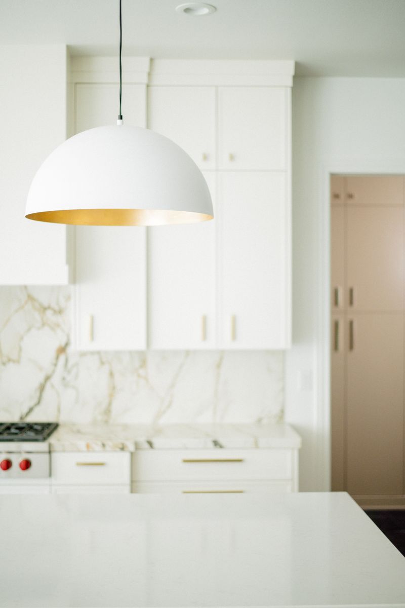 A white kitchen in West Des Moines with a gold lined dome pendant over a marble backsplash.
