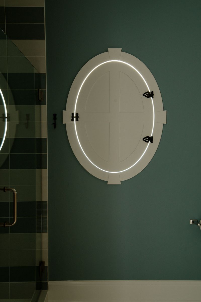 A dark green bath in Panora with a custom pivoting oval window shutter for privacy.