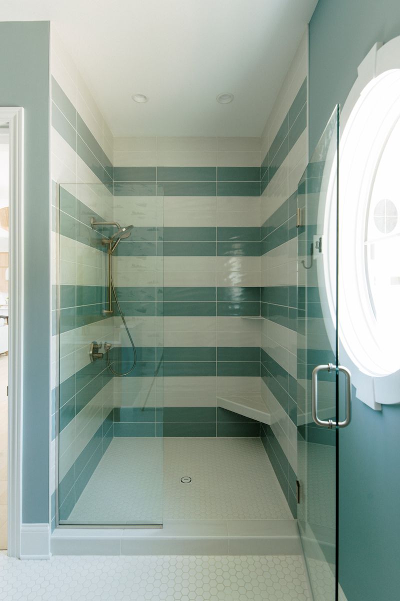 A bathroom in Panora with a walk-in shower tiled in teal and cream stripes and a built-in corner bench.