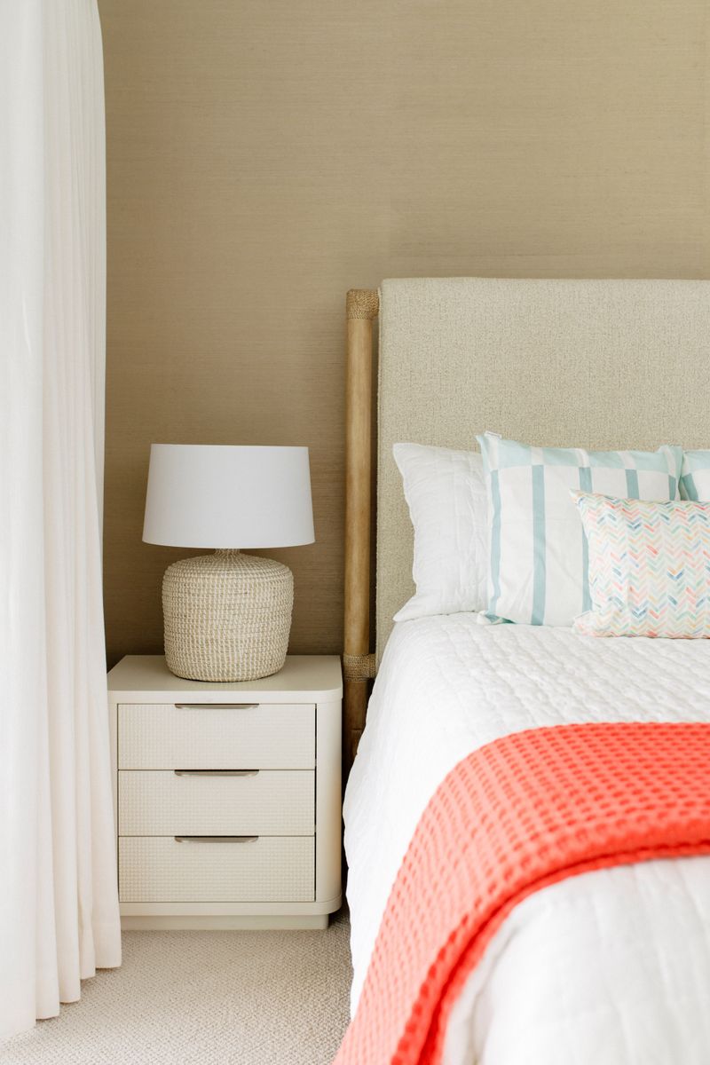 A guest bedroom in Panora with a coral waffle blanket on a white bed and a woven lamp on the nightstand.
