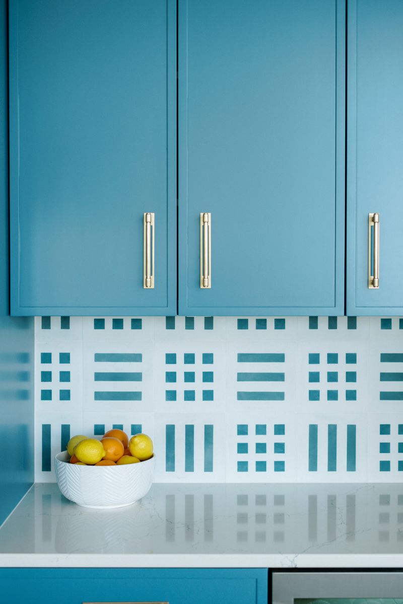 A blue kitchen in Panora with a patterned teal and white tile backsplash above white quartz counters.