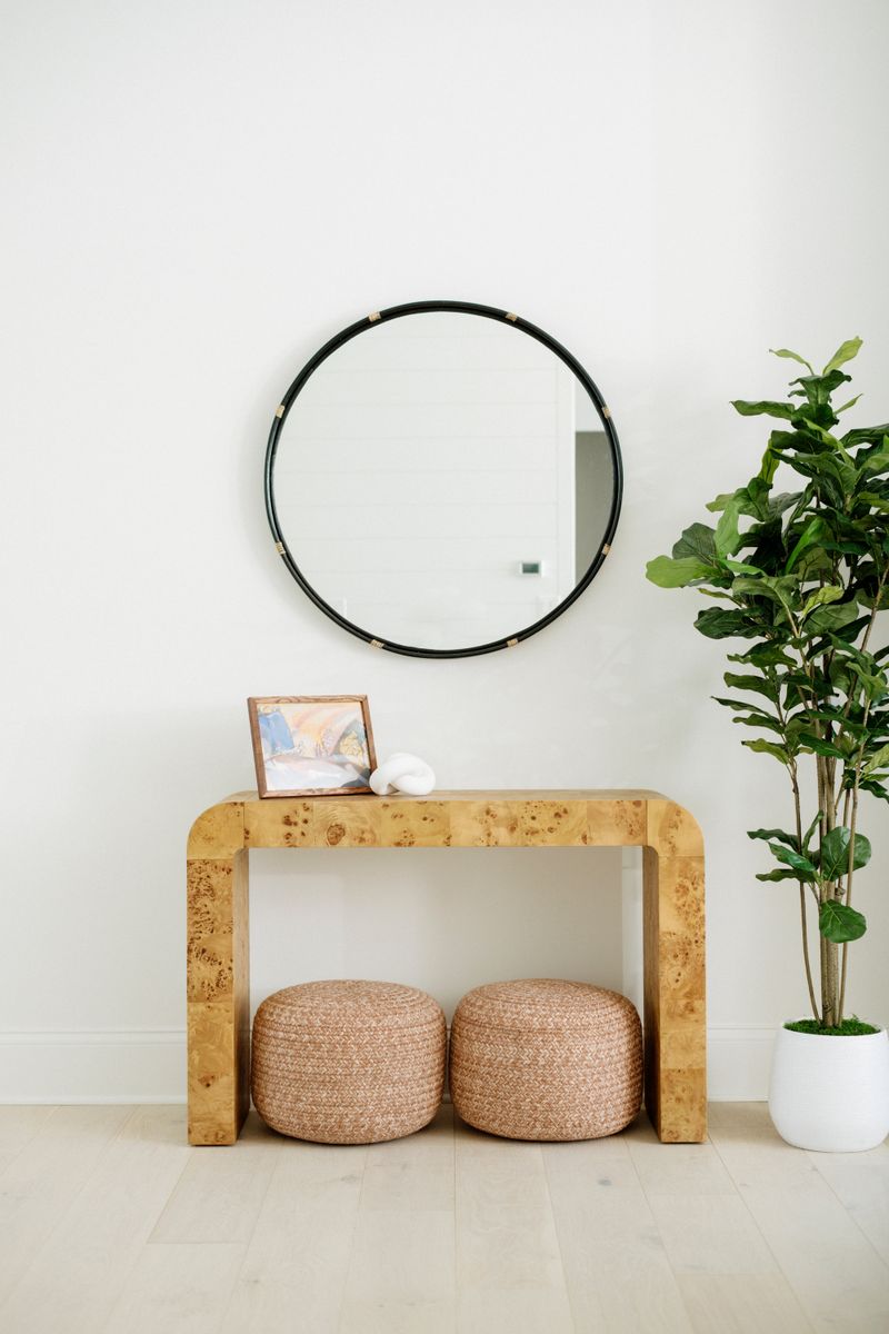 A white entryway in Panora with a round black mirror over a burl wood console table.
